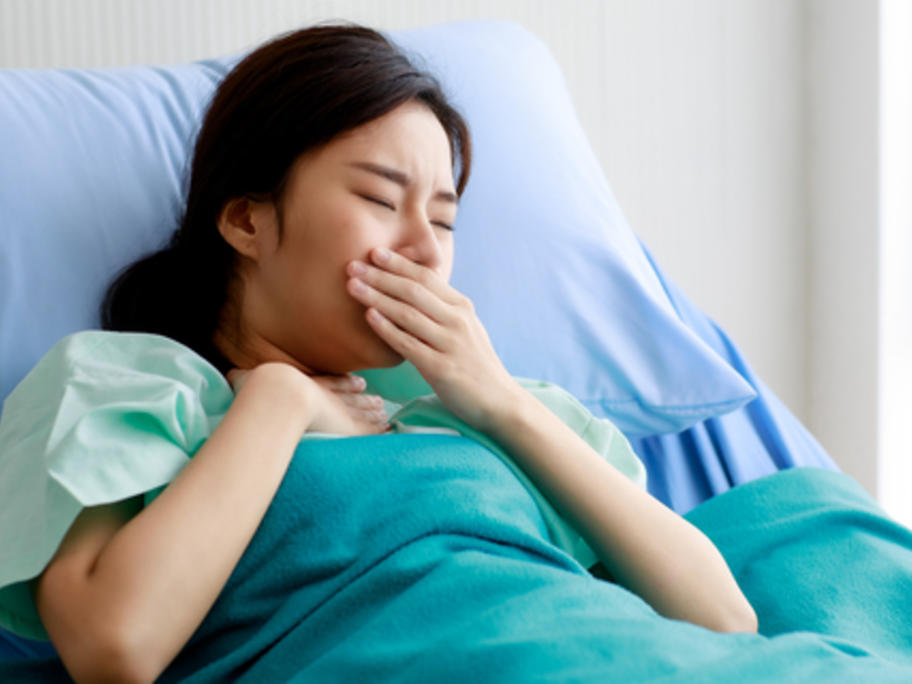 Young Asian woman coughing in hospital bed