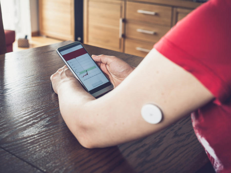 Woman with flash glucose monitoring device on her arm looking at results on her phone