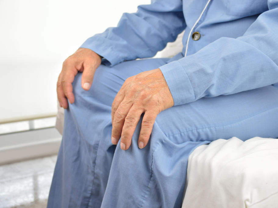 old man in pyjamas sitting on hospital bed