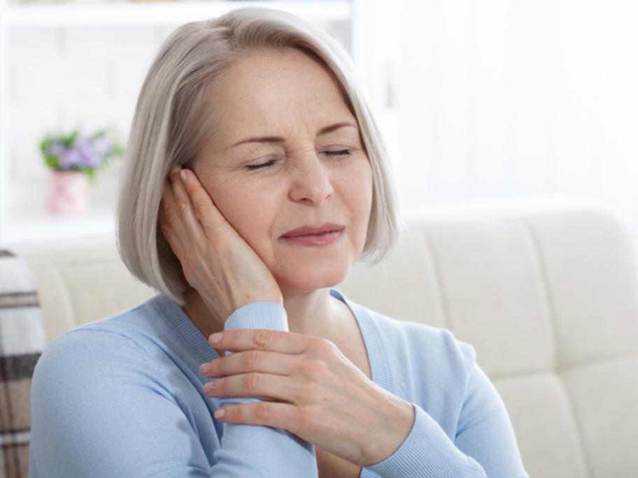 middle aged woman holding ear and looking unhappy - tinnitus
