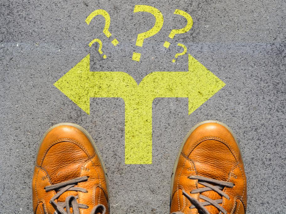 Looking down at a pair of men's feet in shoes and arrows showing a choice to go left or right