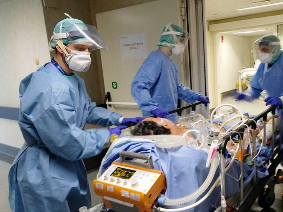 Patient with coronavirus in hospital bed being wheeled by healthworkers wearing PPE