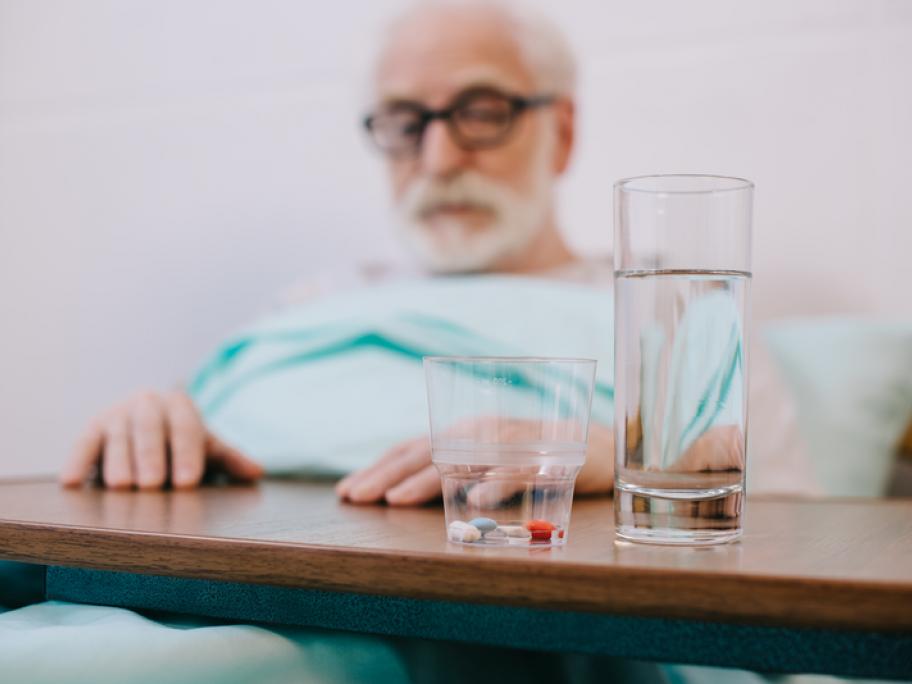 Senior man in hospital with pills and glass of water