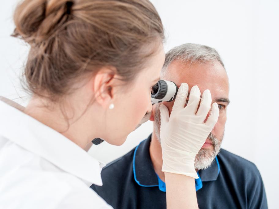 Female doctor checking man's face with dermascope
