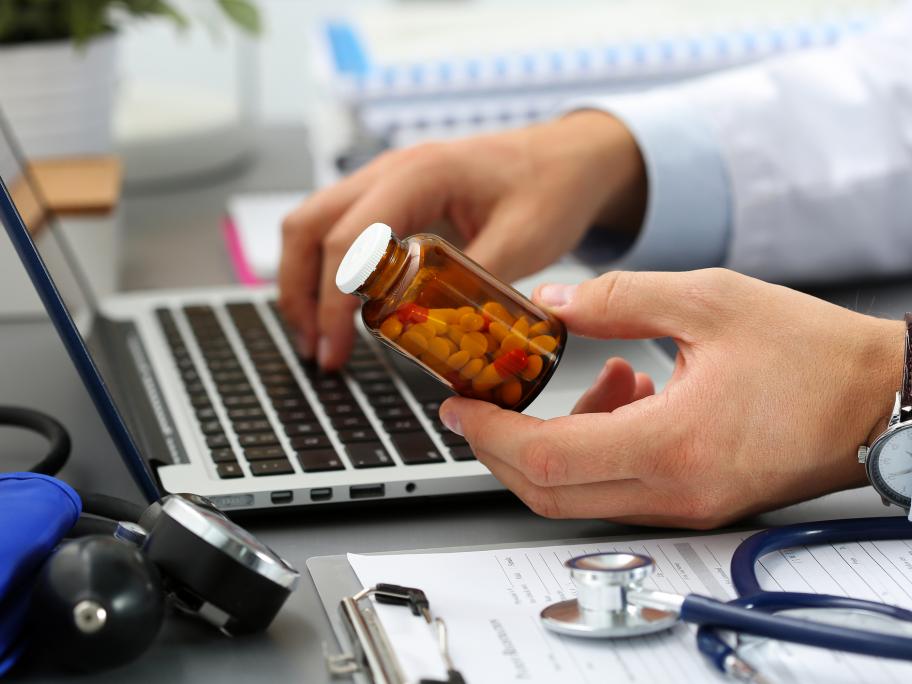 doctor looking up label on pill bottle on his computer